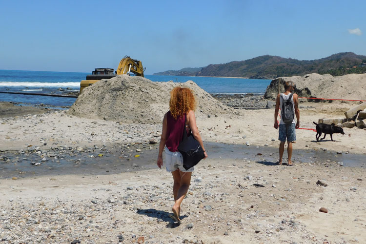 Puente. Comerciantes de alimentos cruzan el arroyo de aguas negras con ayuda de una tabla improvisada para llegar a la zona de bañistas, a solo unos metros de la fuente de descargas. (Fotos: Violeta Meléndez) 